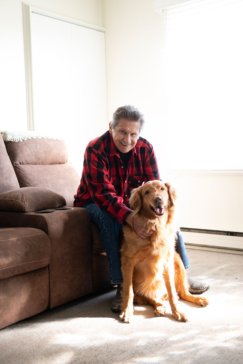 Smiling man and golden retriever sitting together indoors.