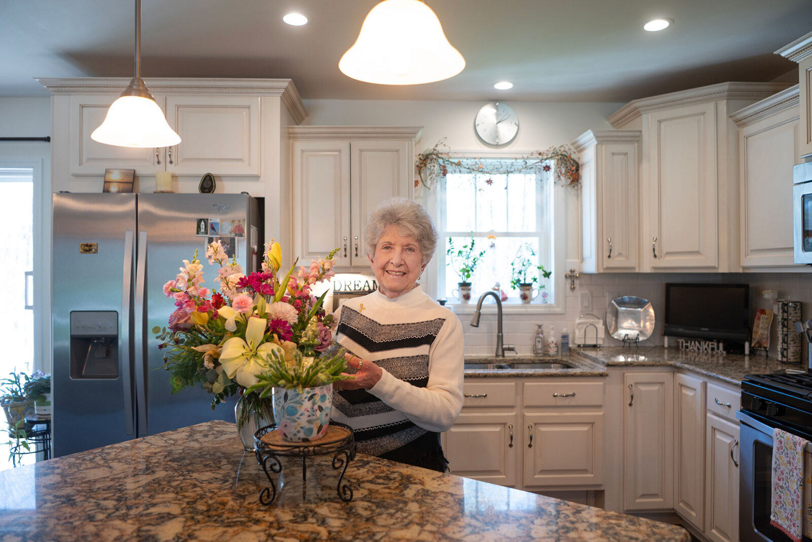 Woman smiling in a bright kitchen with flowers.