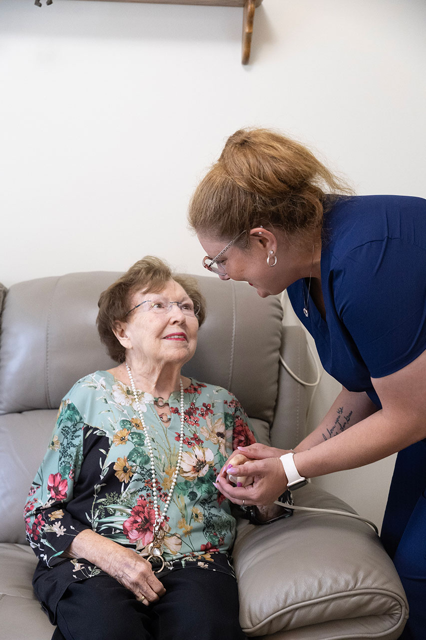 A caregiver interacts with an elderly woman, sharing smiles.