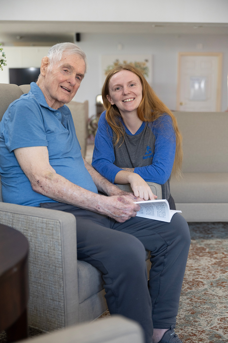 Smiling elderly man and young woman sitting together indoors.