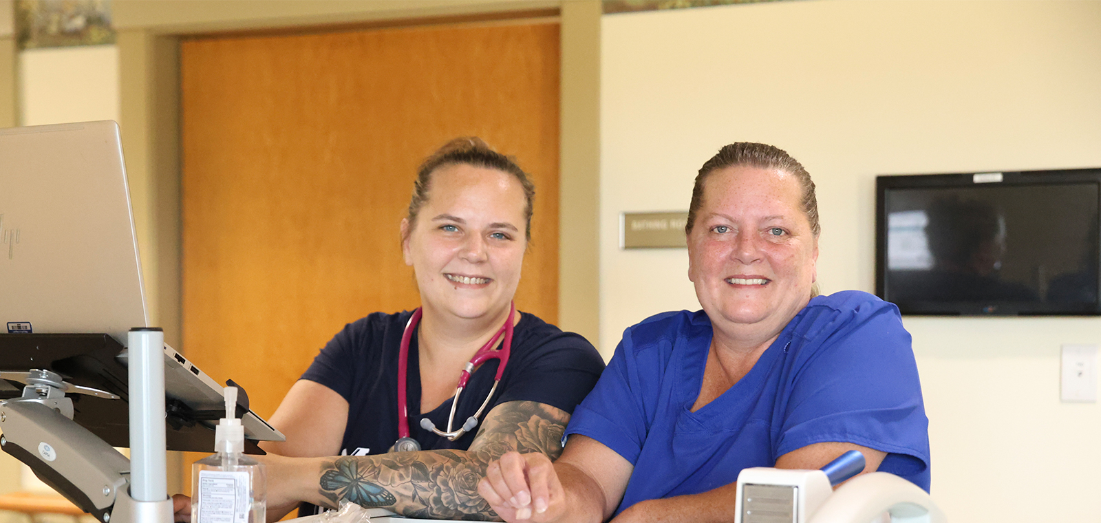 Two healthcare workers smiling in a bright environment.