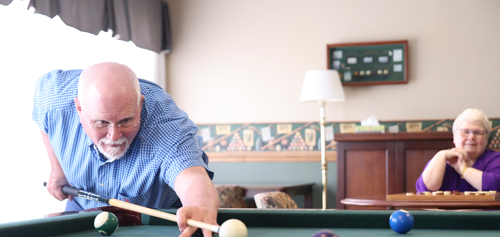 Man playing pool, woman watching, relaxed indoor setting.