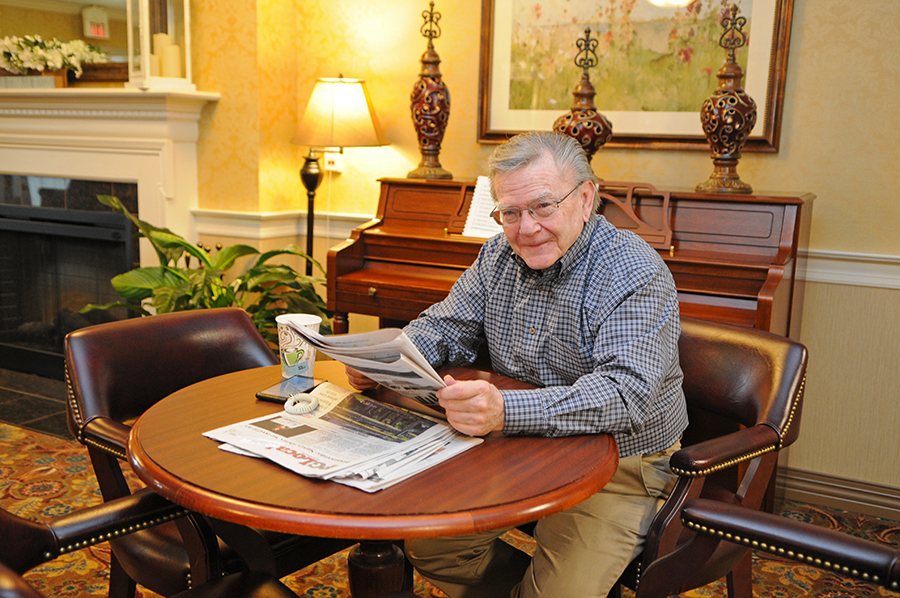 Older man reading a newspaper in a cozy setting.