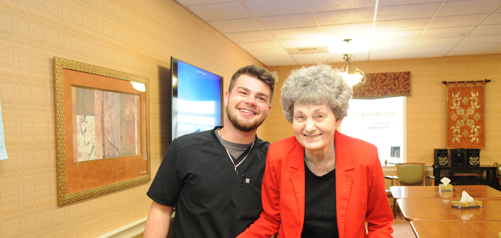 Smiling young man with elderly woman in a bright setting.