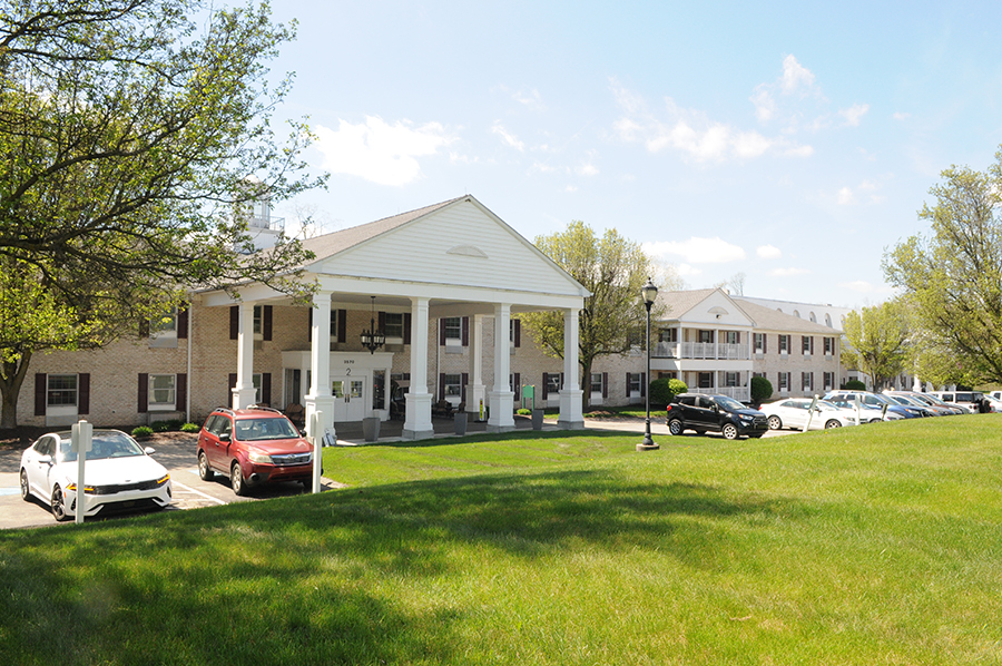 Two-story building with columns, cars, and grassy area.
