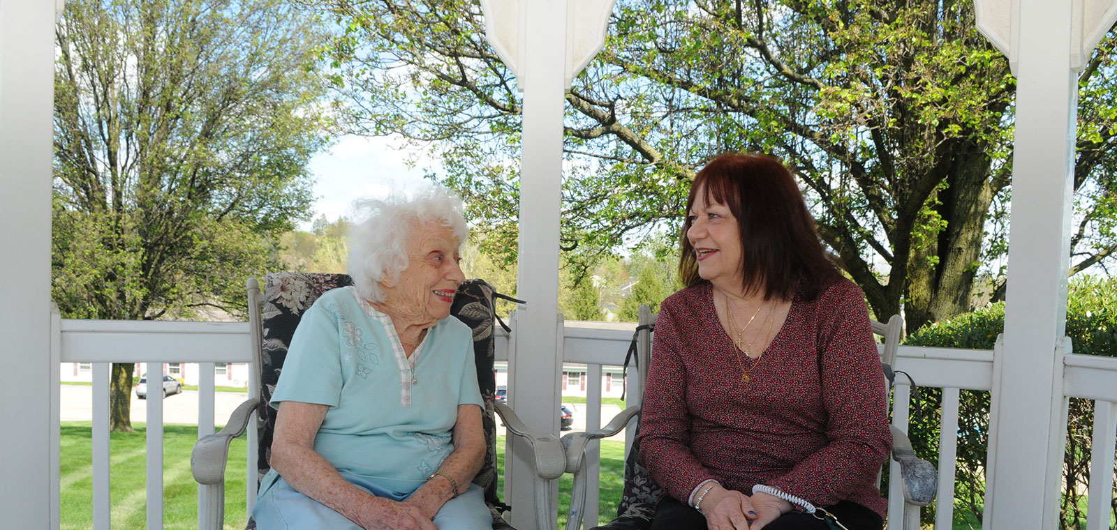 Two women smiling and talking on a porch.