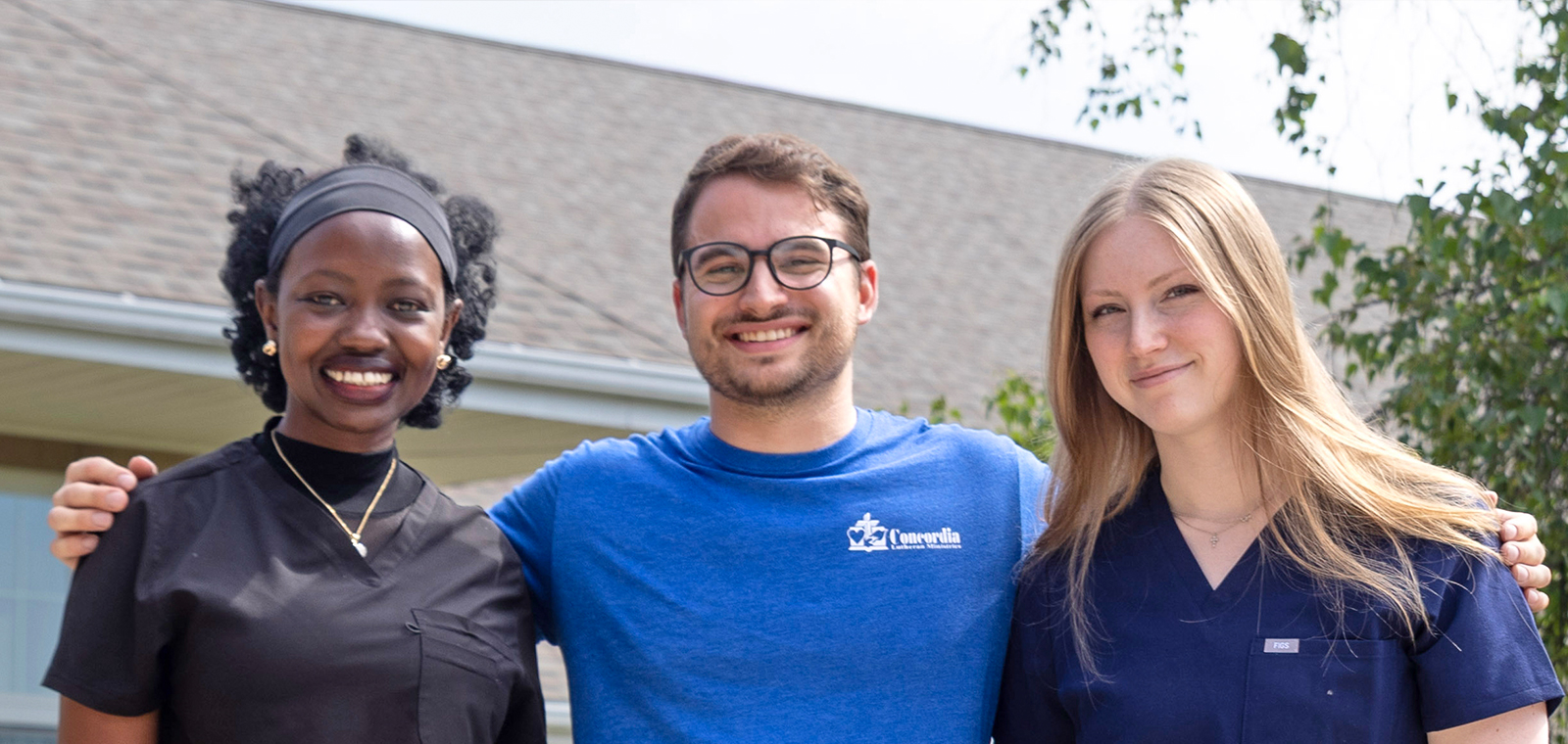 Three smiling individuals in medical attire outdoors.