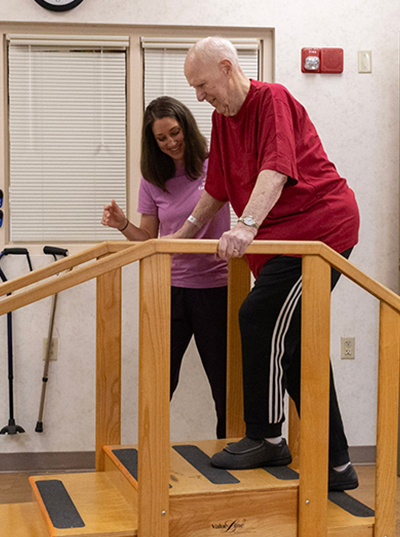 Therapist assists elderly man on wooden stairs.