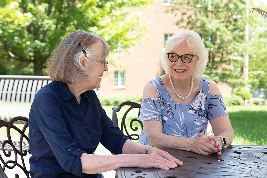 Two women enjoying sunny day, smiling and chatting outdoors.