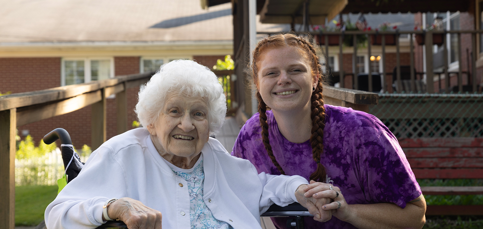Smiling elderly woman and young woman outdoors, holding hands.