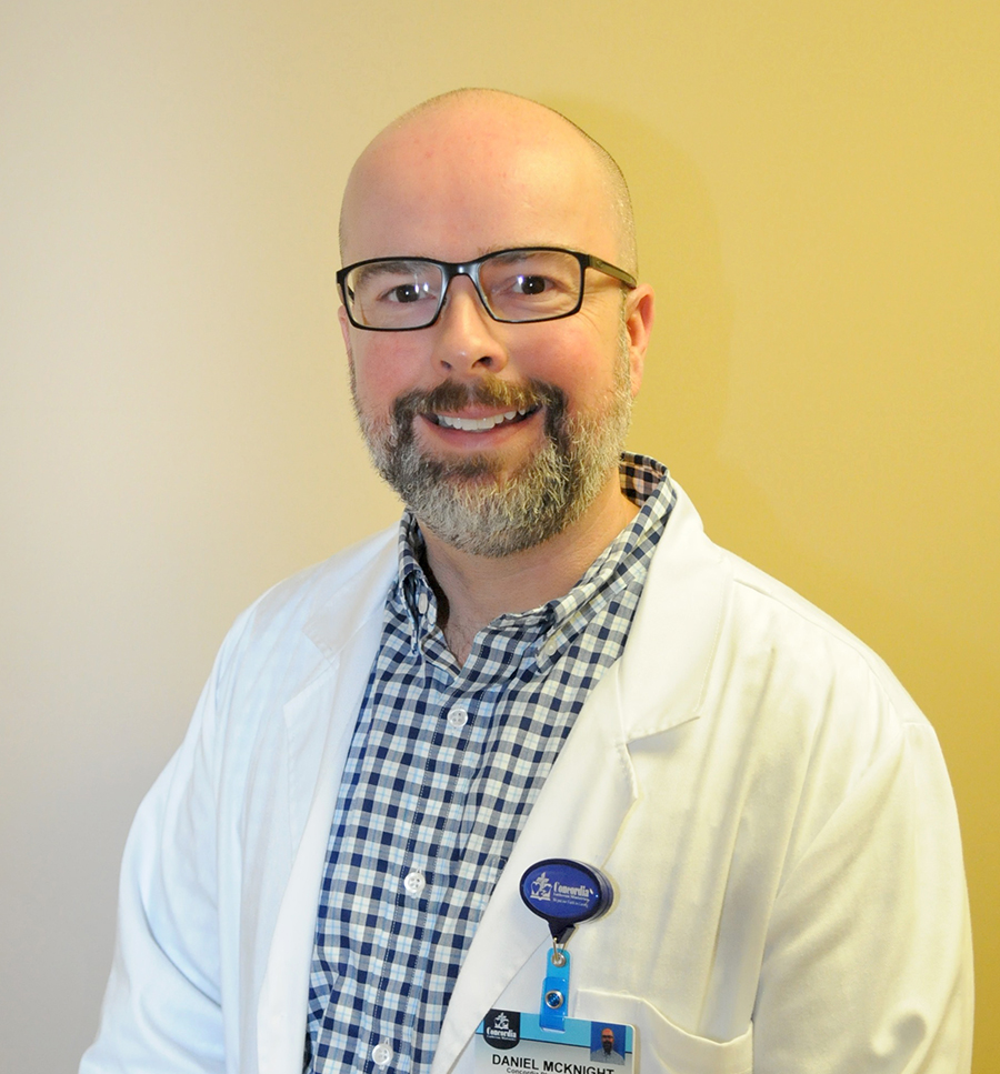 Man in white coat, smiling, with glasses and badge.