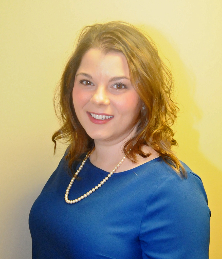 Woman smiling, wearing blue dress and pearl necklace.