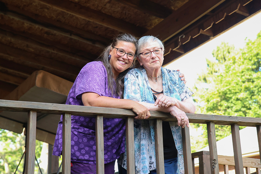 Two women smiling together on a porch railing.