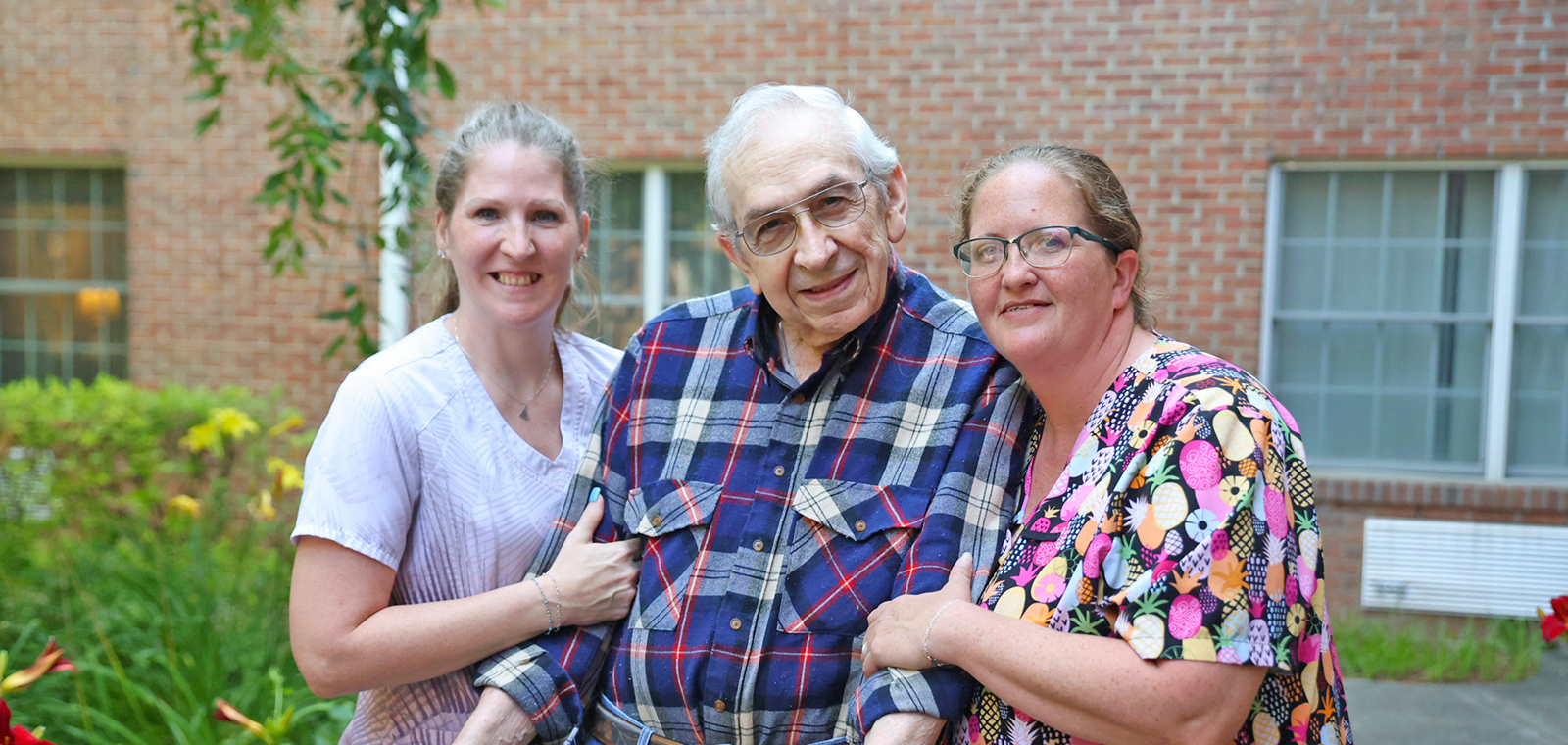 Three people smiling together in a garden.