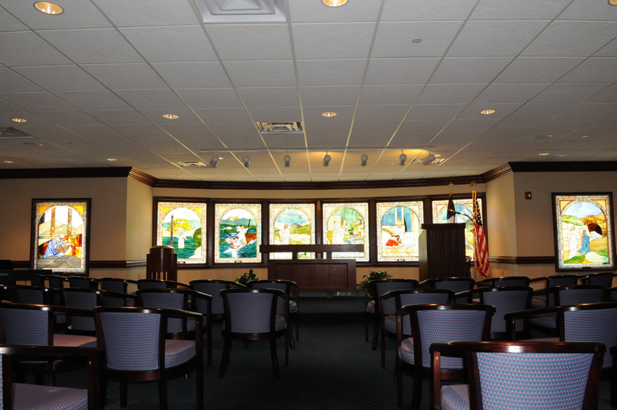 Chapel with stained glass windows and seating arrangement.