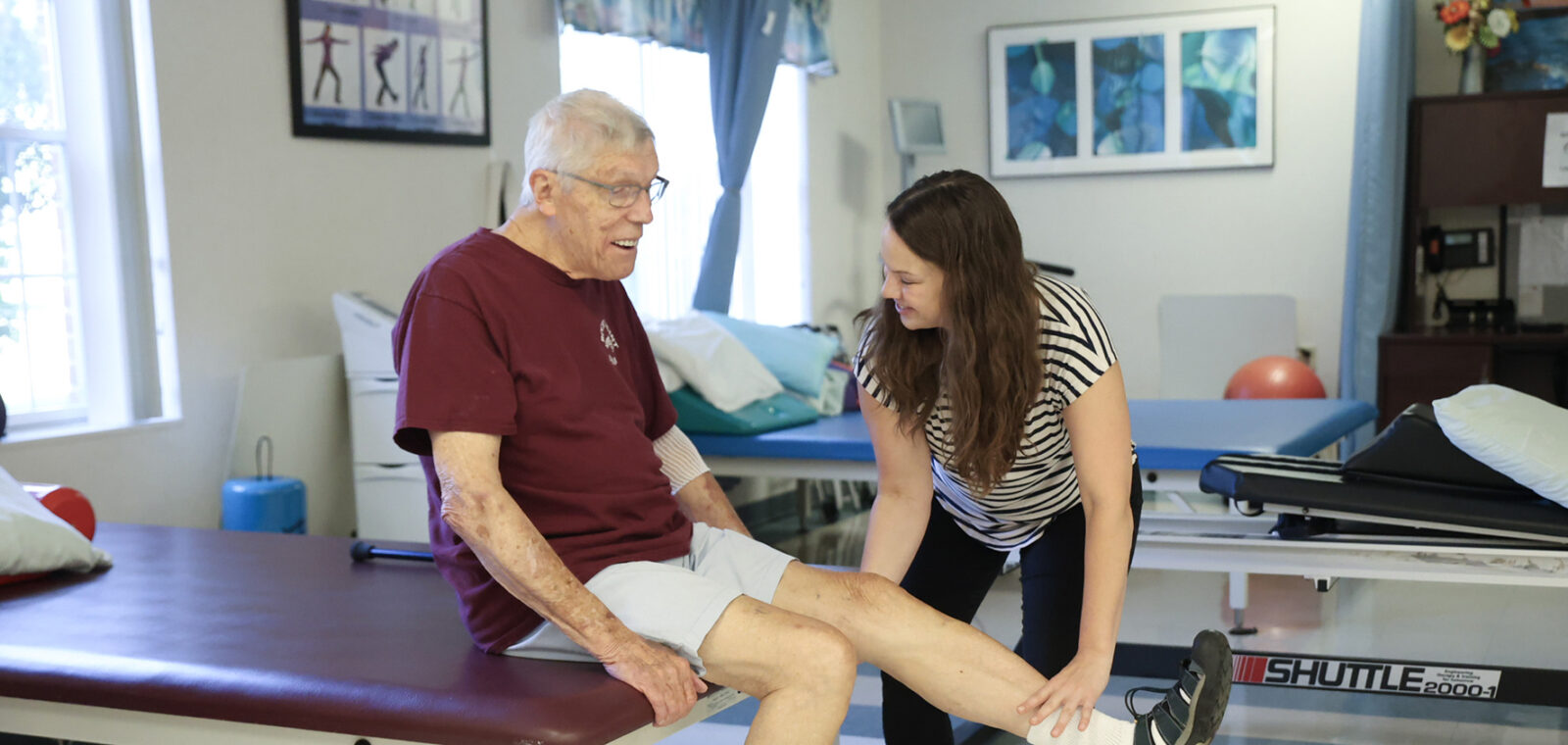 Physical therapy session between an elderly man and therapist.