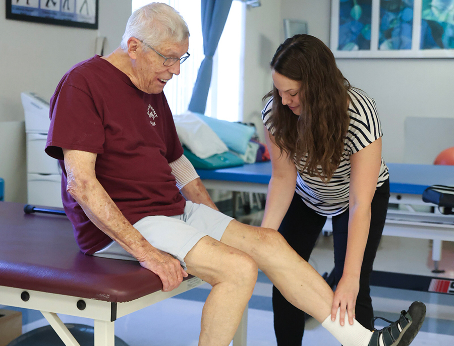 Elderly man receiving physical therapy from a young woman.