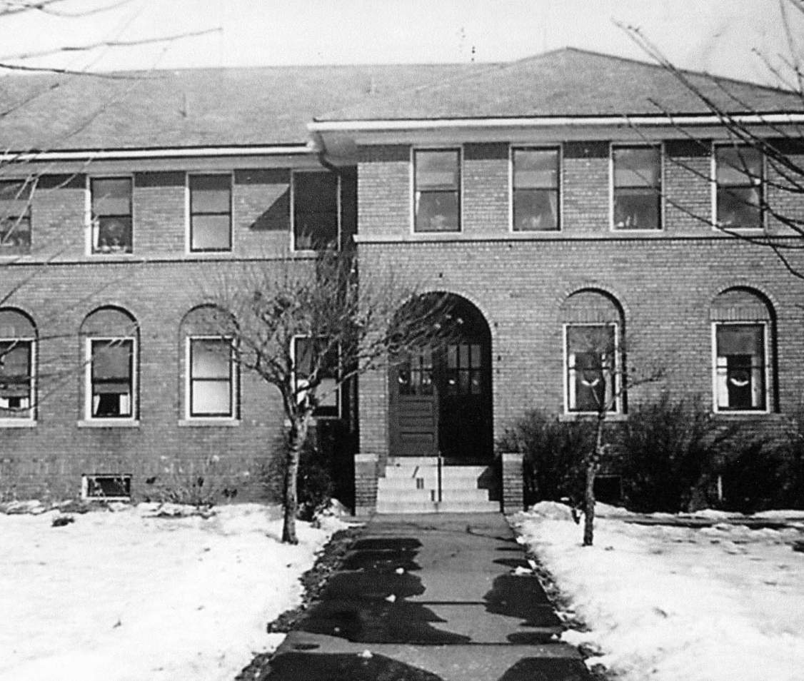 Two-story brick building with snow-covered ground and trees.