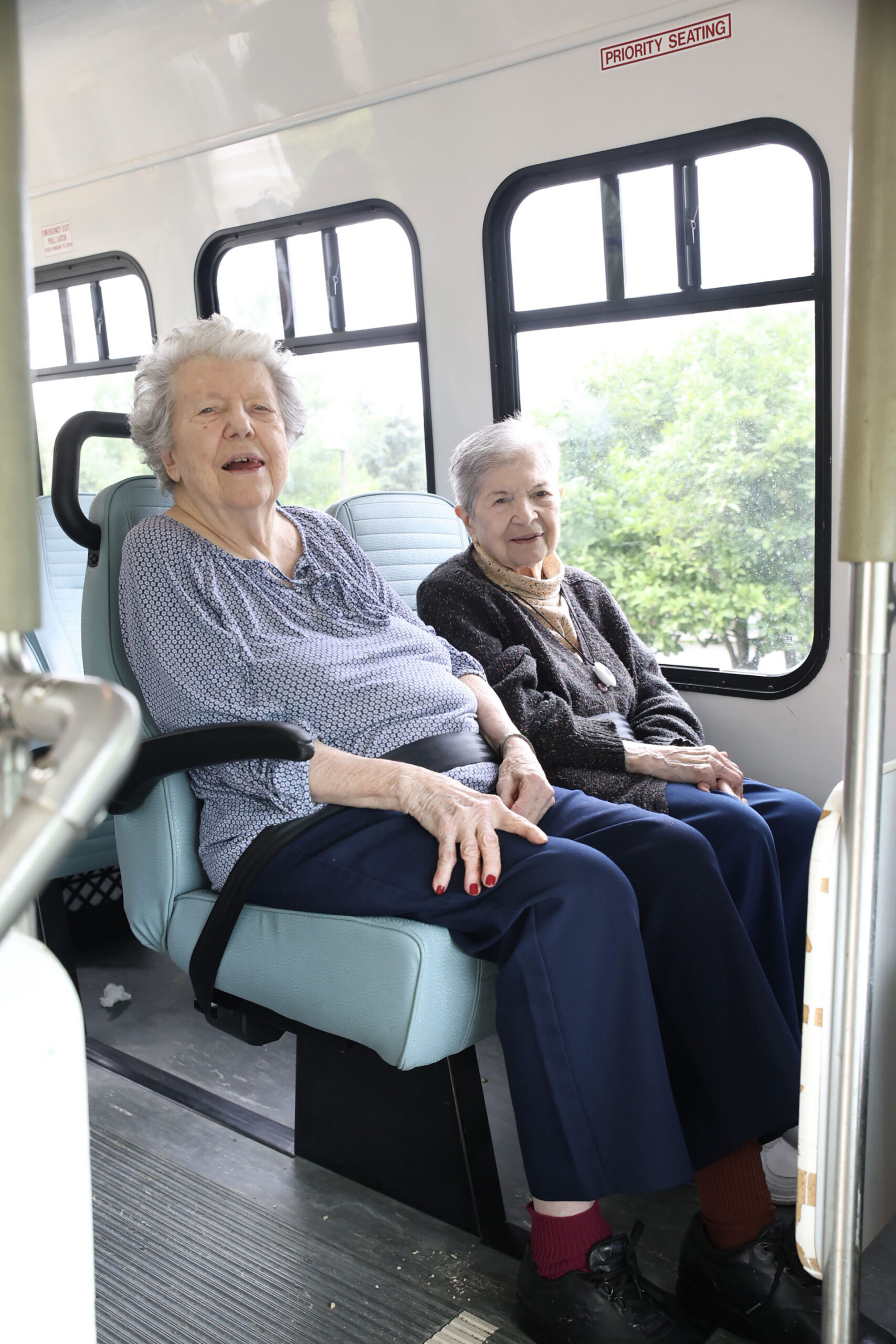 Two elderly women sitting on a bus, smiling.