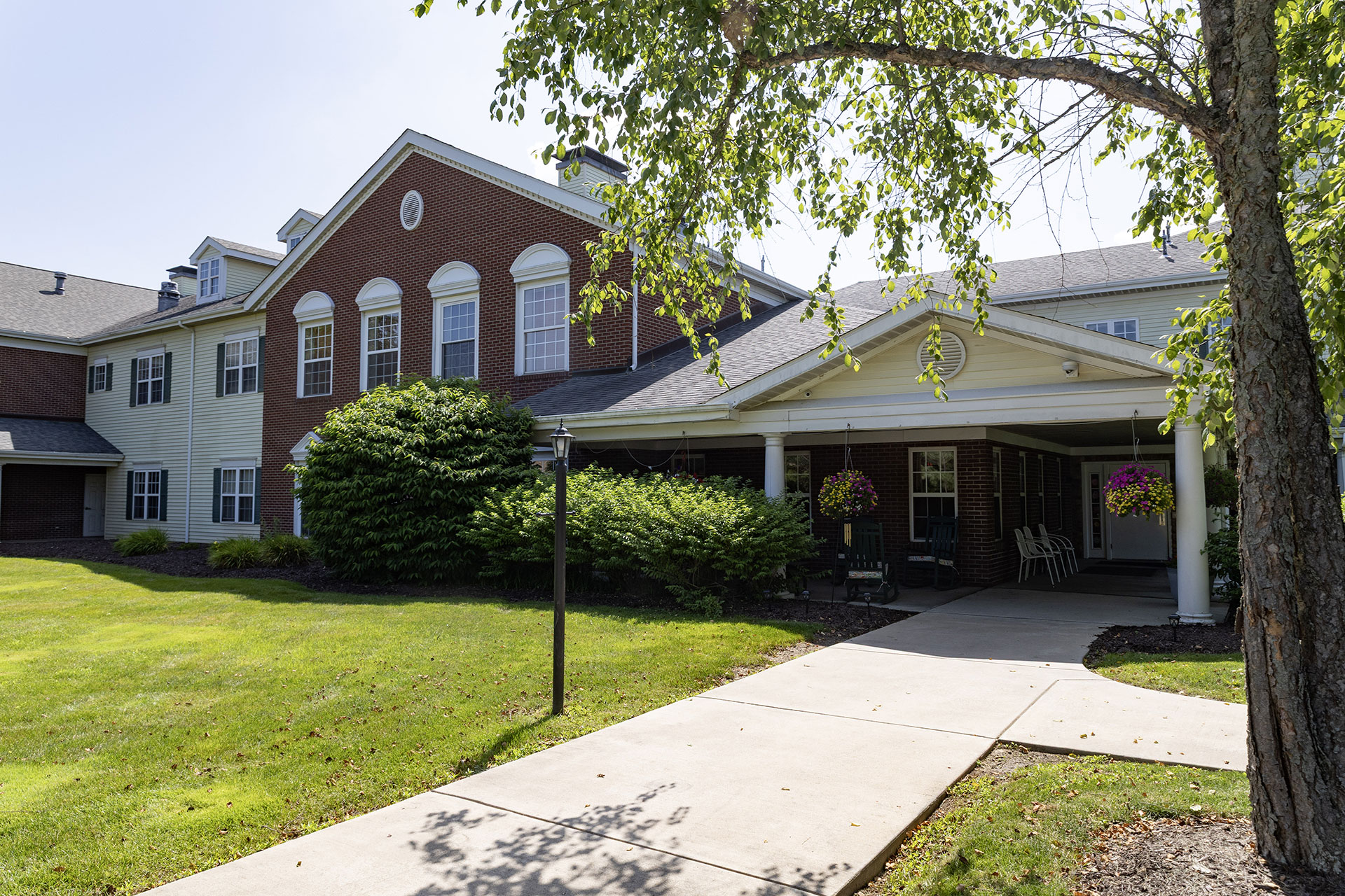 Brick building with greenery, pathway, and flower baskets.