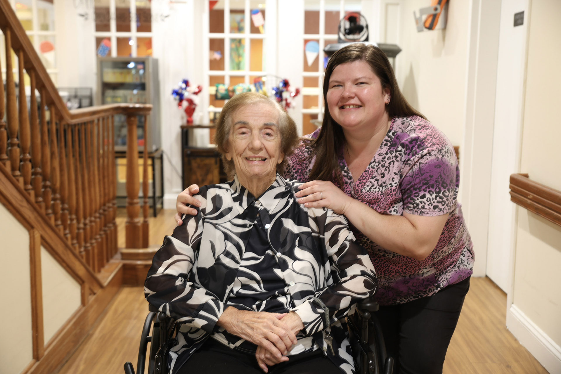 Two women, one in a wheelchair, smiling together indoors.