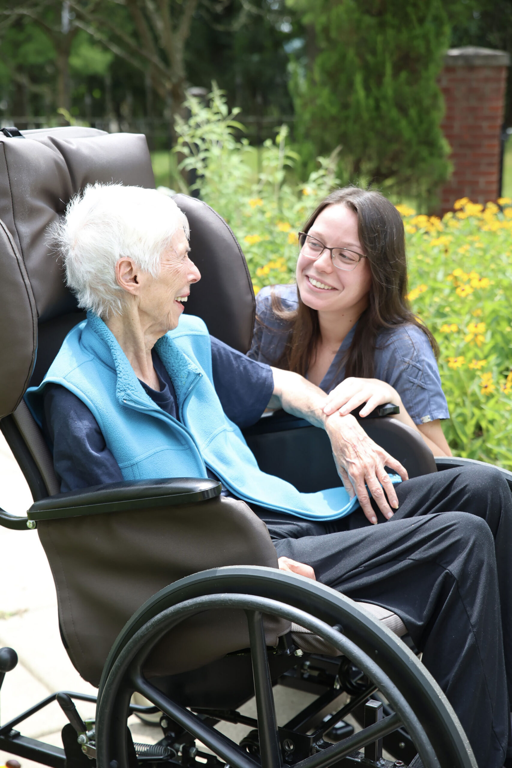 Two women share a joyful moment outdoors in a wheelchair.
