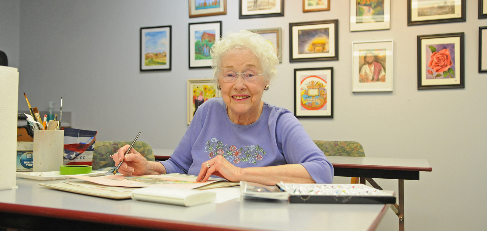 Elderly woman painting in a colorful, art-filled room.