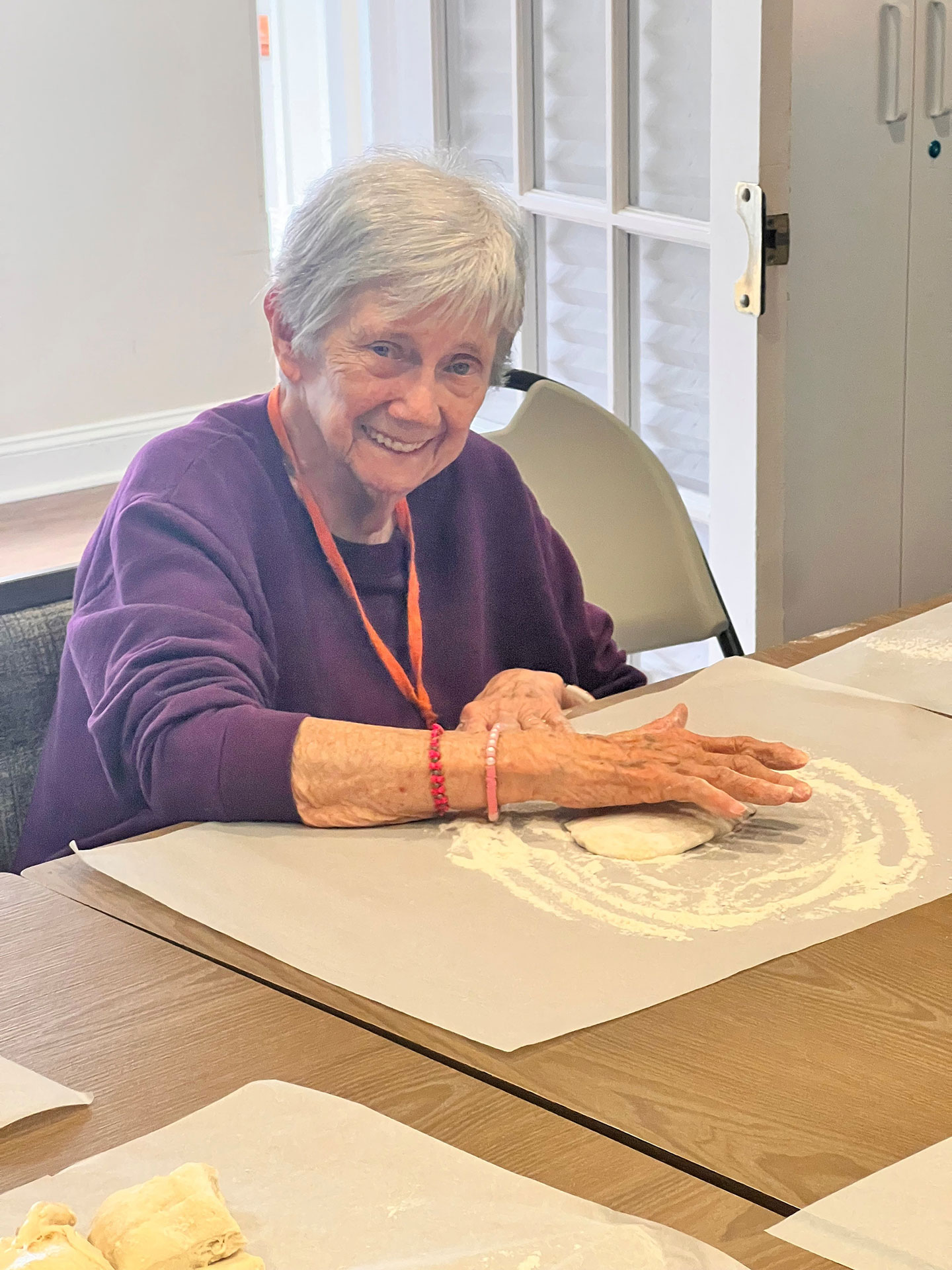 Elderly woman smiling while baking with dough on table.