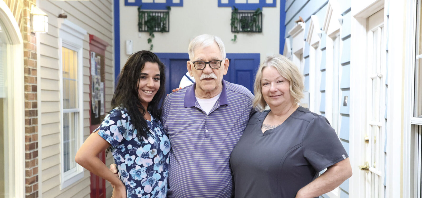 Three people smiling together in a brightly decorated hallway.