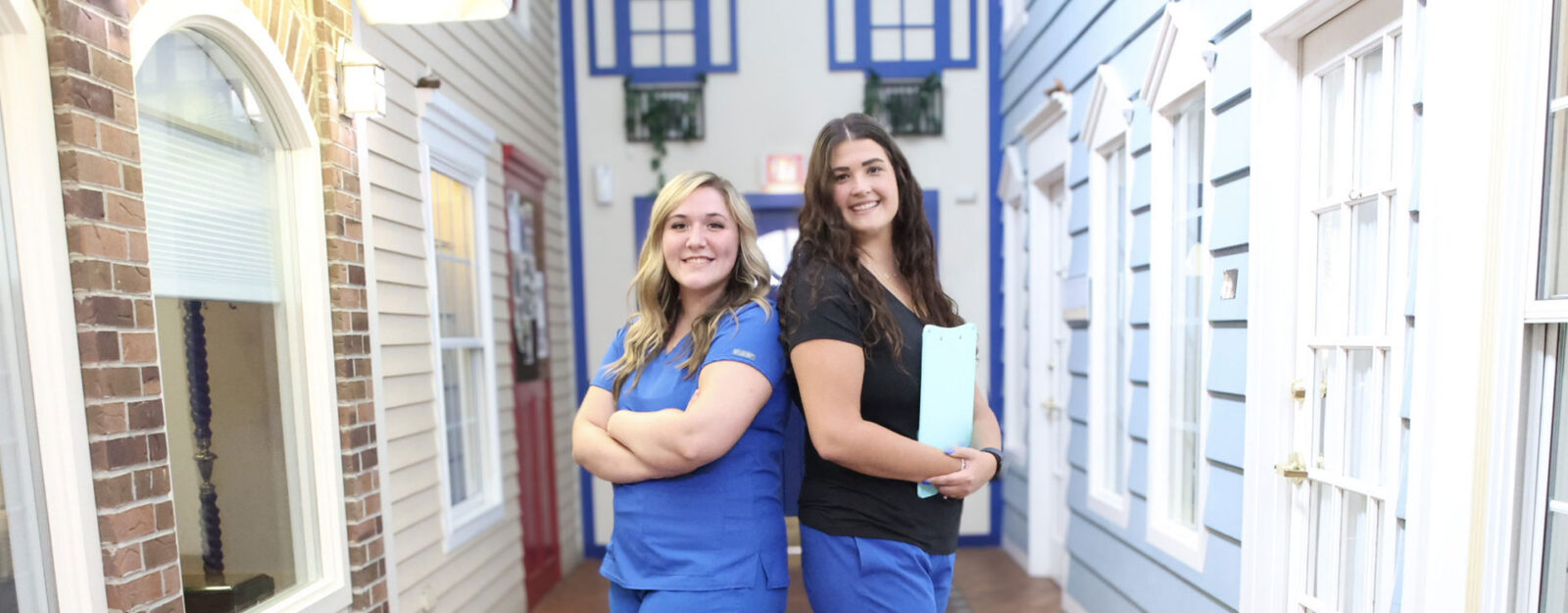 Two women in scrubs posing in a corridor.
