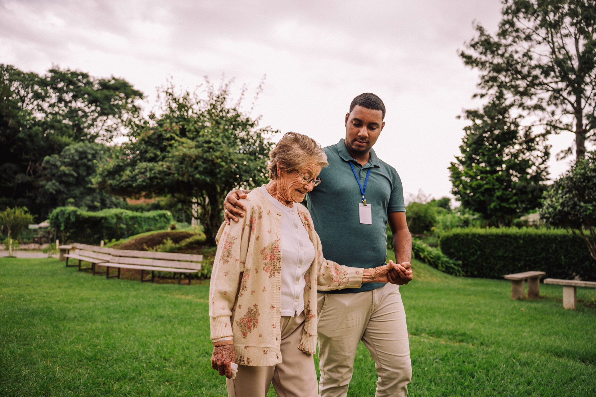 Caregiver assisting an elderly woman in a garden.