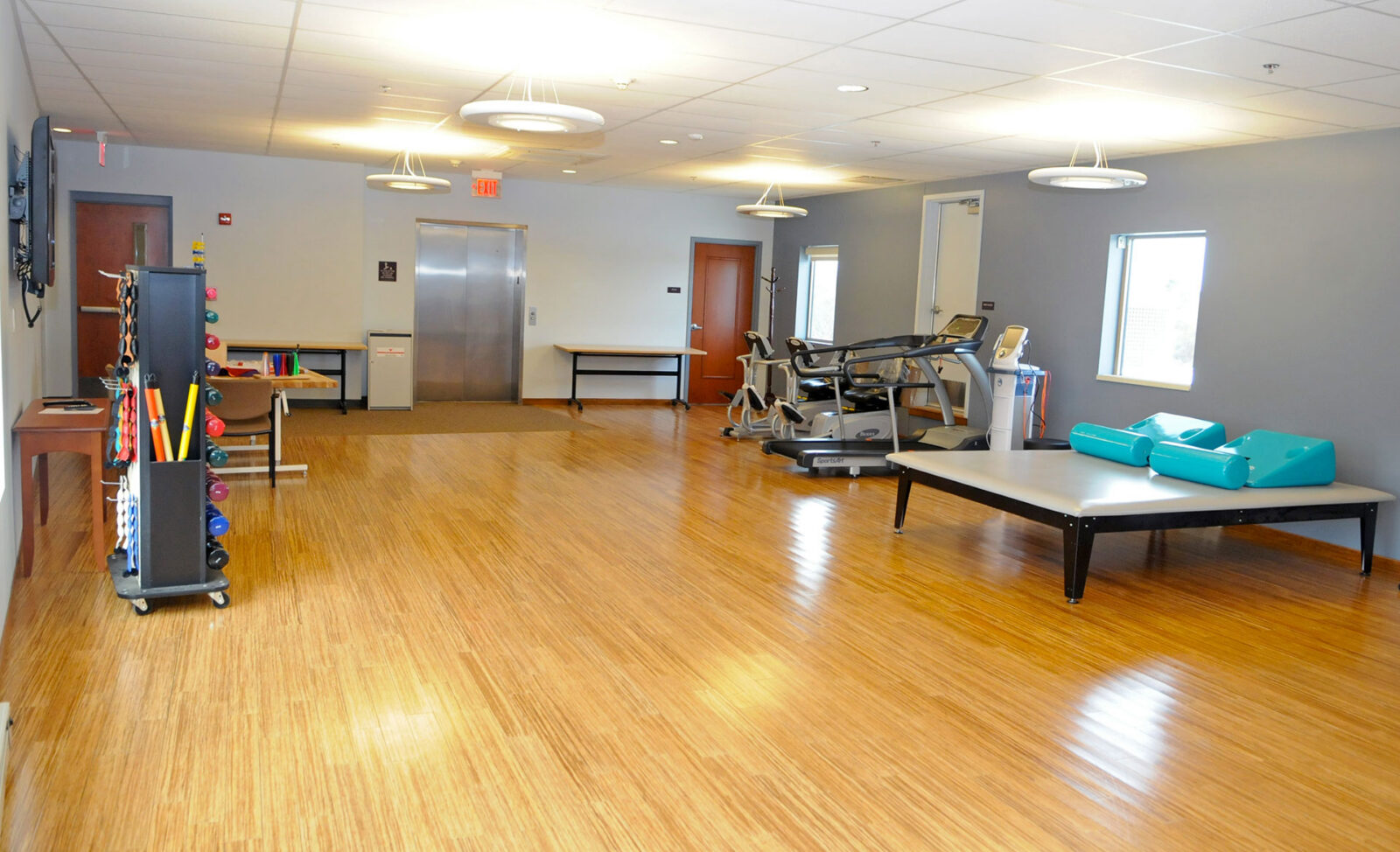Bright therapy room with exercise equipment and wooden flooring.