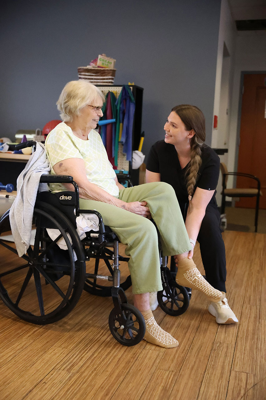 Caregiver assists elderly woman in a wheelchair.
