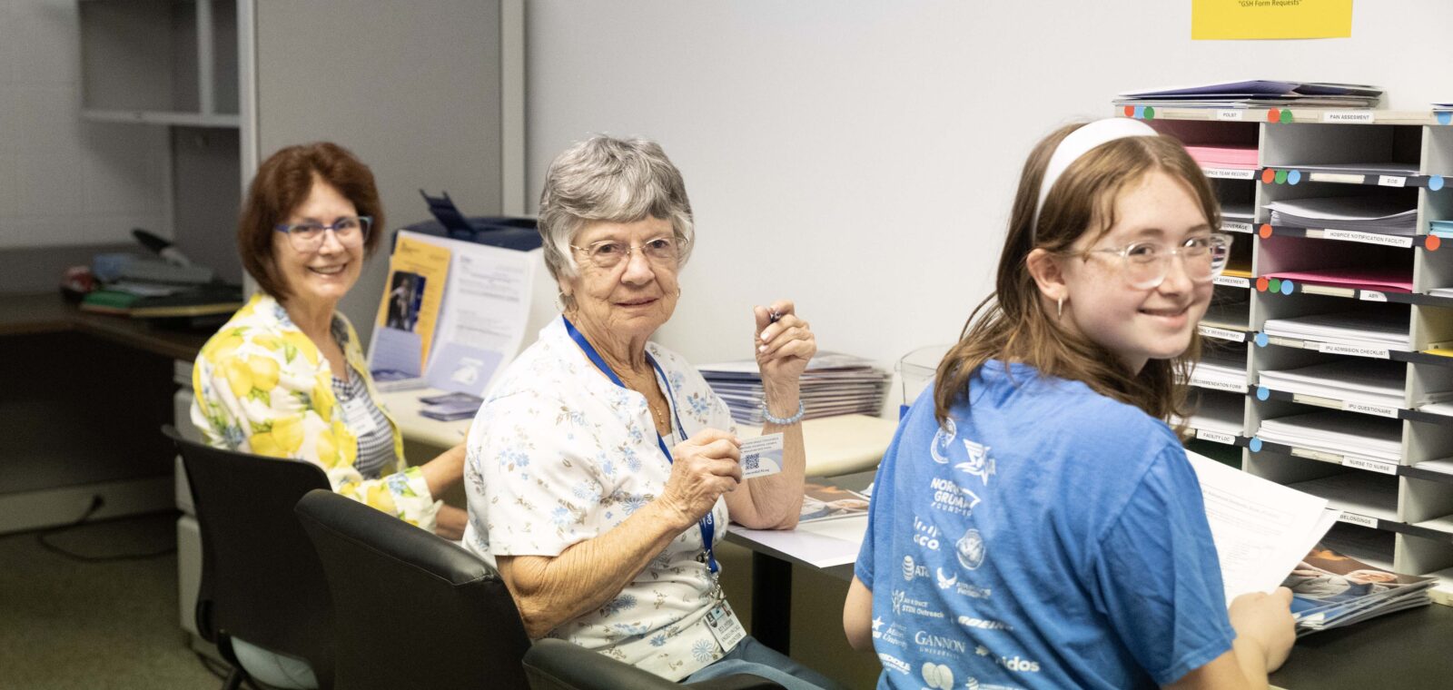 Three women and a girl working at desks, smiling.