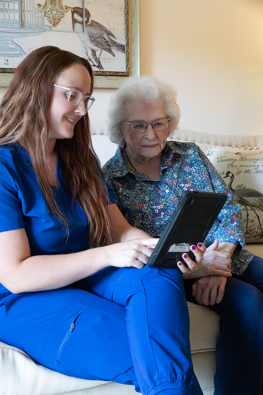 Caregiver and elderly woman sharing a tablet experience.