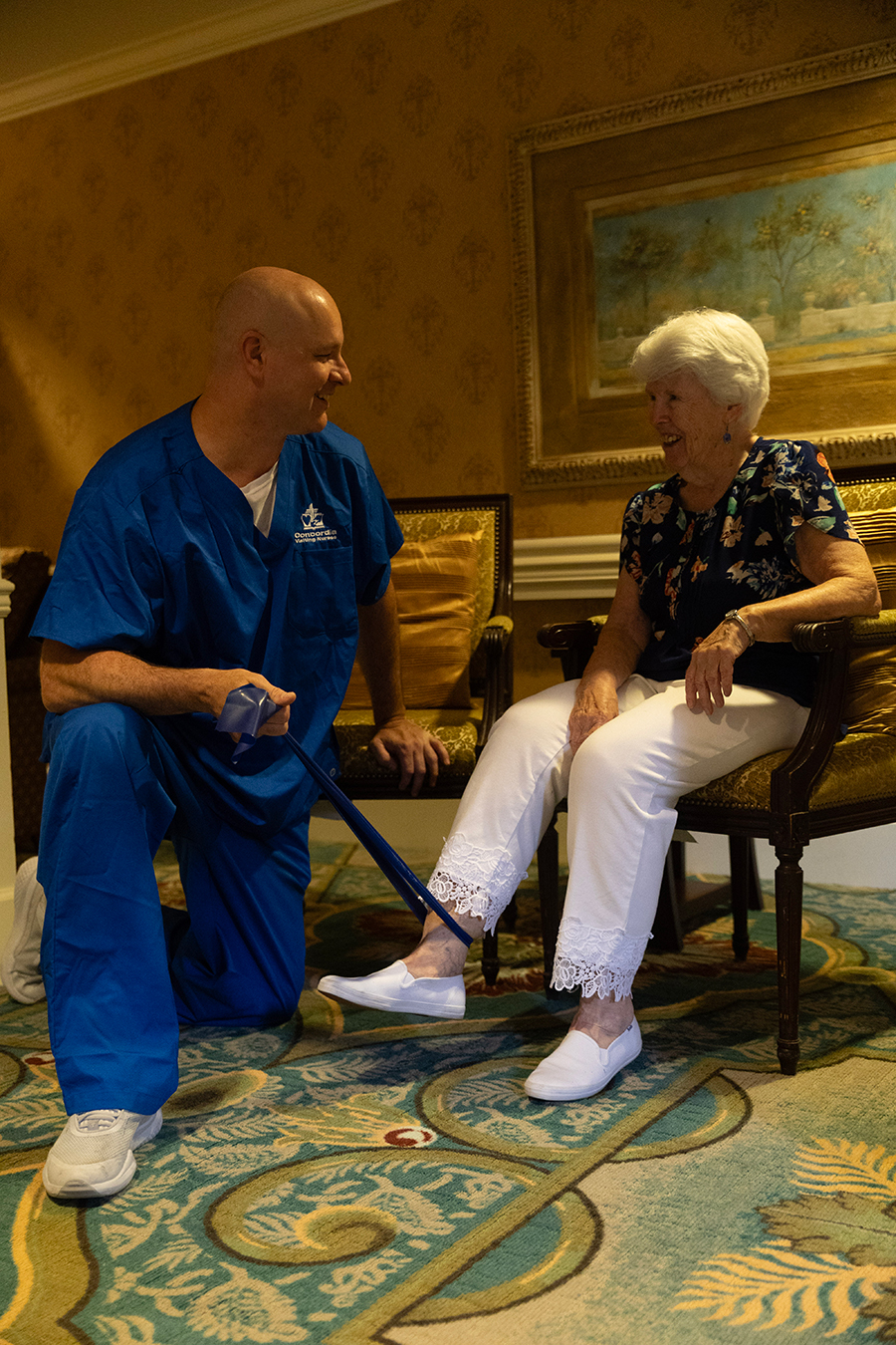 Man assisting an elderly woman in a care setting.