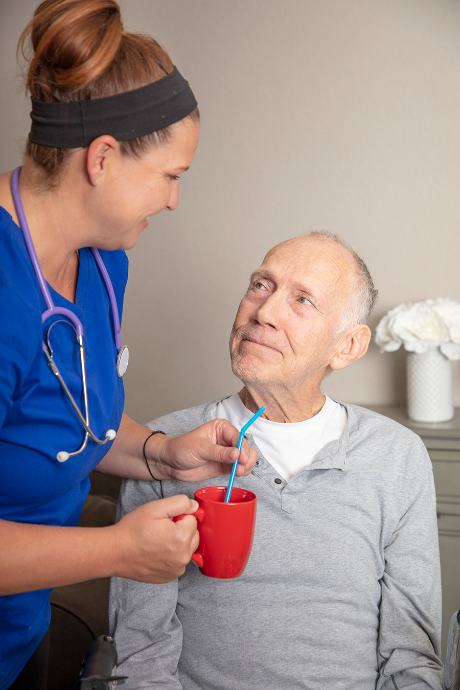 Nurse assisting an elderly man with a drink.