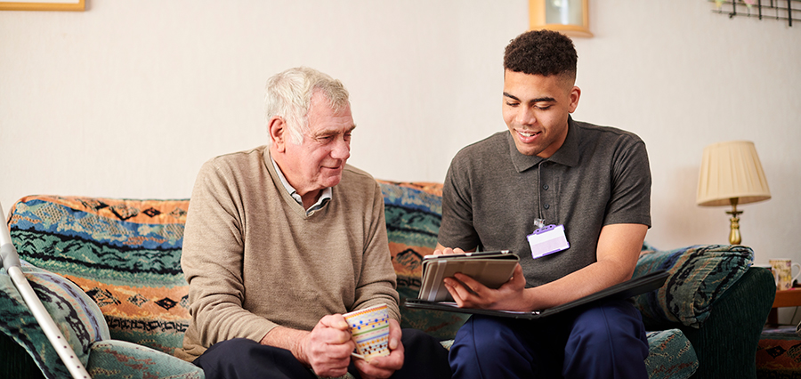 Caregiver assisting elderly man in a comfortable living room.