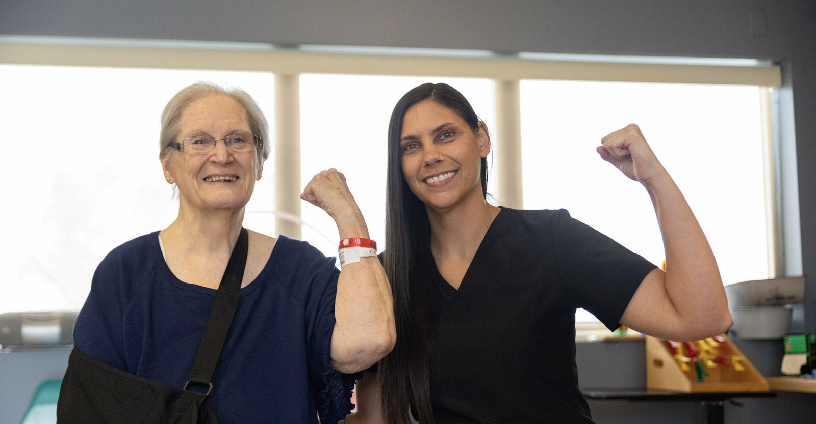 Smiling woman and therapist flexing muscles, celebrating strength together.