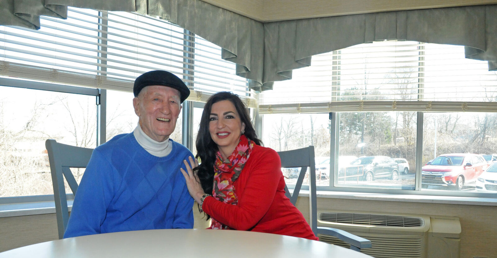 Smiling couple seated by a window, bright and cheerful setting.