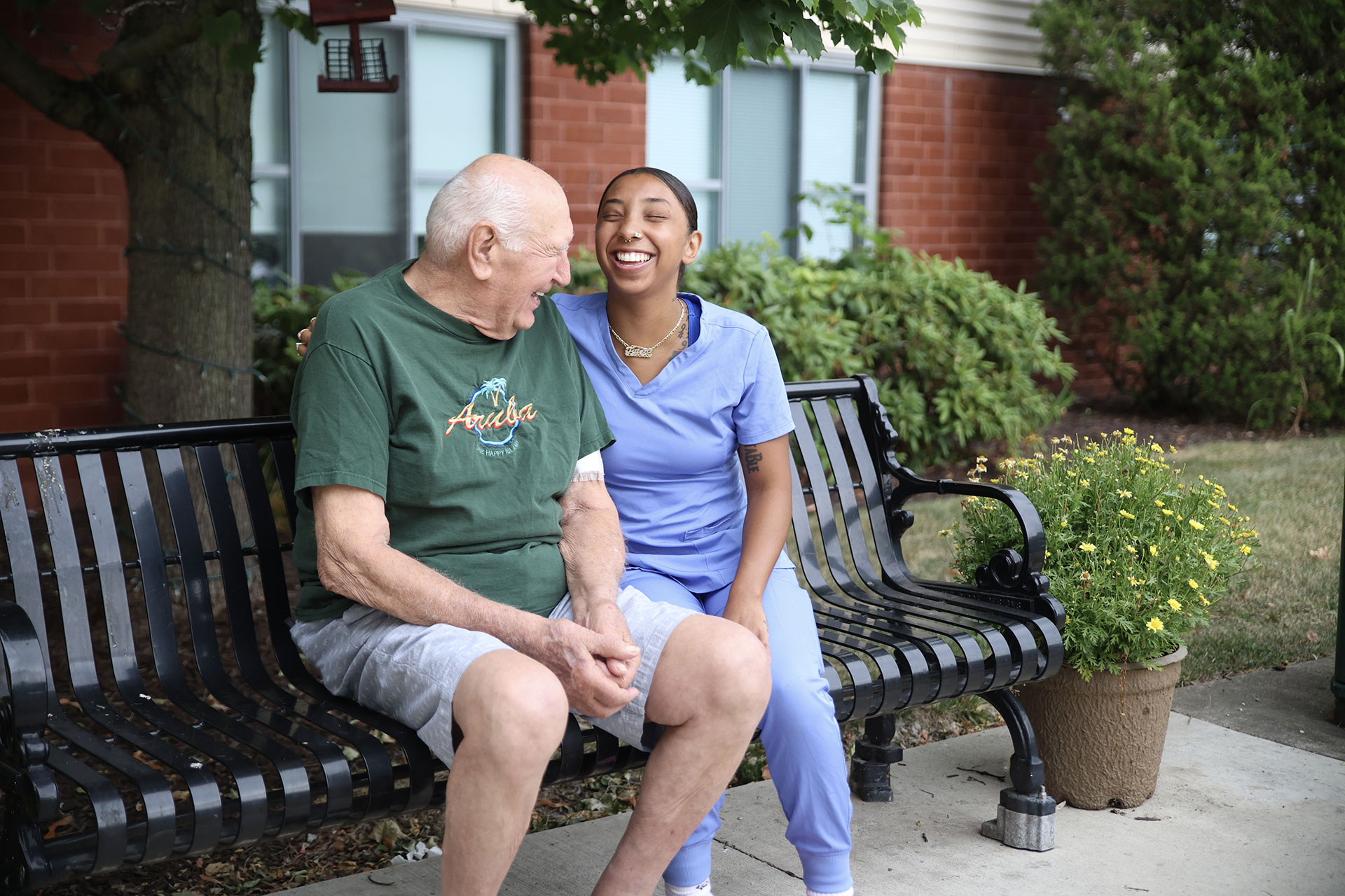 Elderly man and young woman laughing together on a bench.