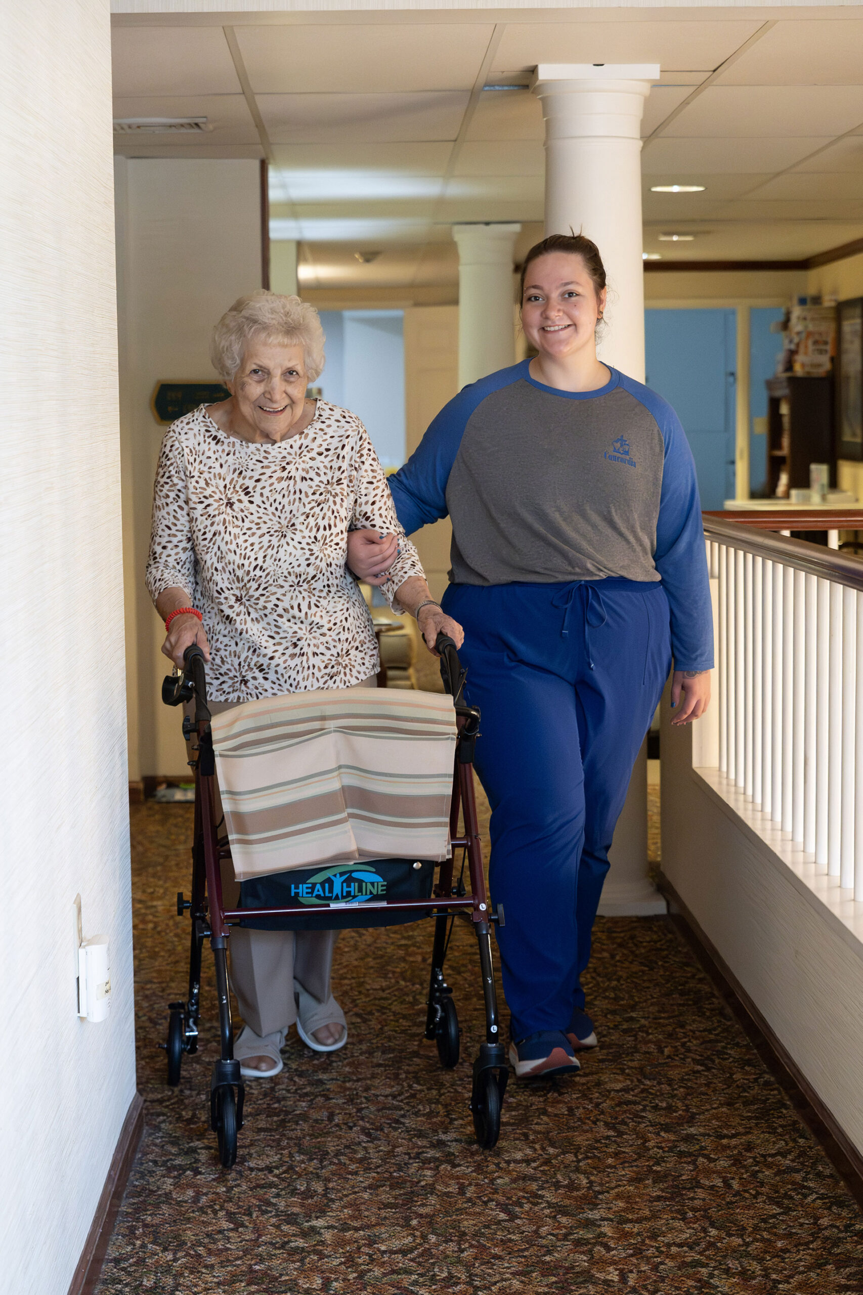 Older woman with walker assisted by a younger caregiver.