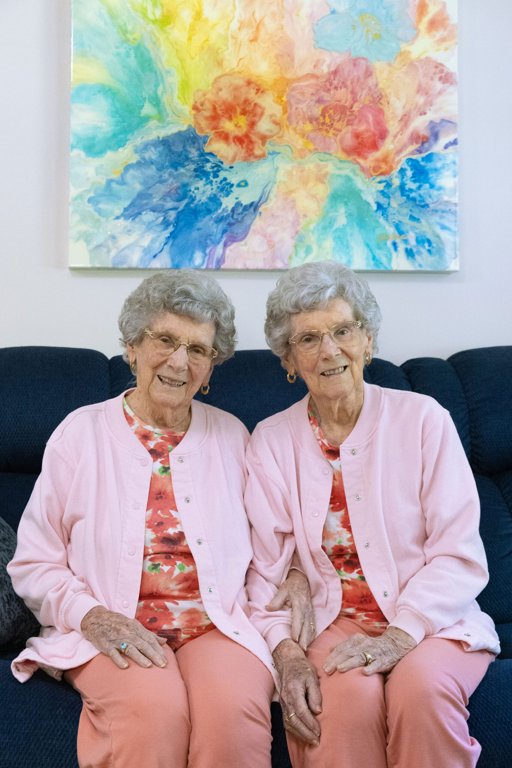Twin sisters sitting together, smiling, in pastel outfits.