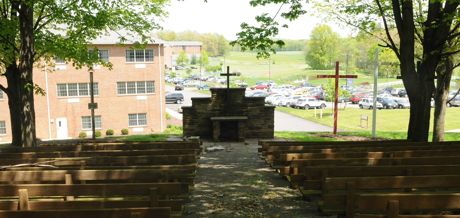 Outdoor chapel with seating and crosses, surrounded by greenery.