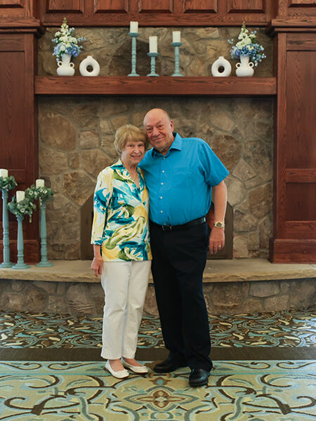 Couple poses happily by a stone fireplace indoors.