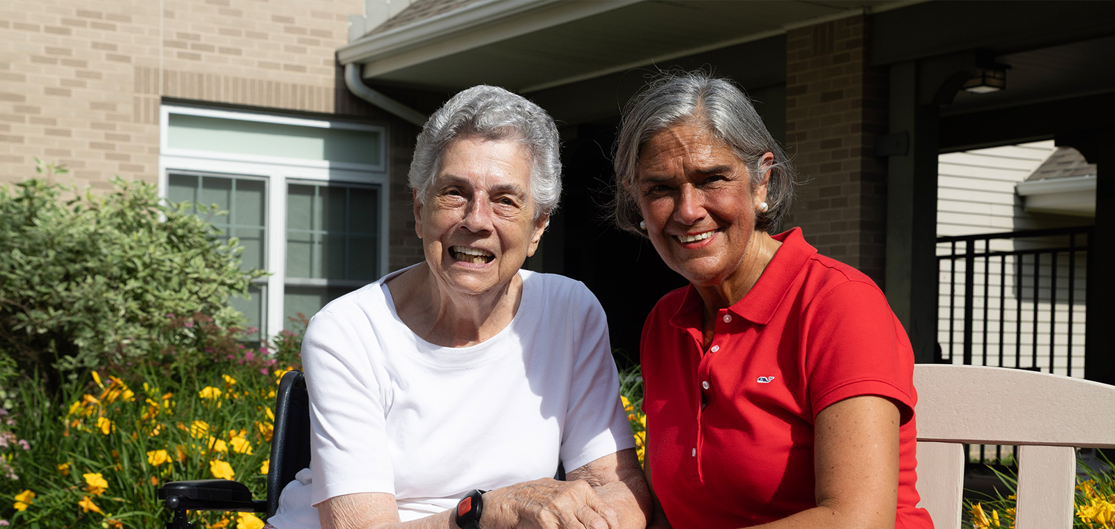Two smiling women enjoy time together in a garden setting.