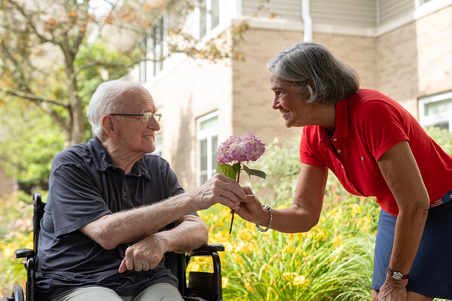 Man in wheelchair receiving flowers from smiling woman.