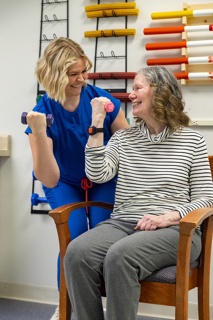 Therapist and senior woman exercising with dumbbells and smiling.