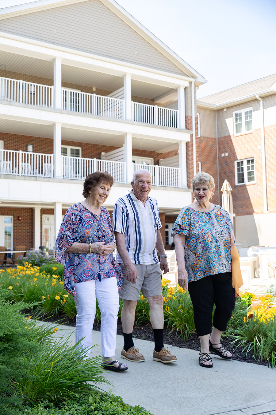 Three seniors walking joyfully outside a residential building.