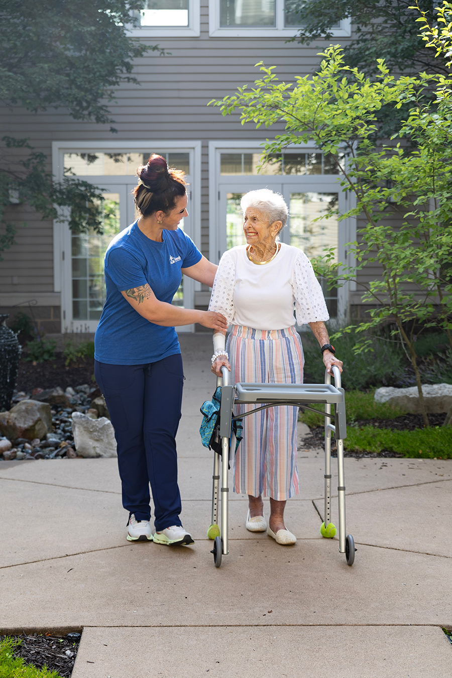 A caregiver assists an elderly woman with a walker.